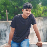 Man wearing a Supima Cotton black t-shirt and blue jeans sitting outdoors with greenery in the background