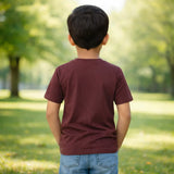 Child wearing a marron suvin gold cotton plain t-shirt and blue jeans standing in a park with trees and grass.