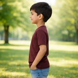 Young boy standing in a park wearing suvin gold cotton plain burgandy tees with trees and grass in the background