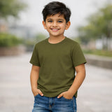 Child wearing an olive green t-shirt and blue jeans standing outdoors with a blurred background