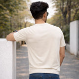 Man in a  off-white suvin gold cotton t-shirt standing outdoors with trees in the background