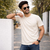 Man wearing off white  suvin gold cotton t-shirt leaning against a wall outdoors.