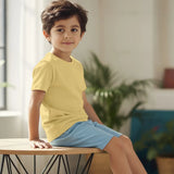 Child wearing a yellow shirt and blue shorts sitting on a table indoors.